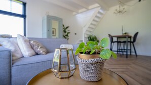 A modern living room with a grey sofa, a coffee table with a potted plant, and a dining area in the background. - Neu:wunderschöne und Preiswerte Ferienwohnung mit Jedem Komfort (Westhoek)