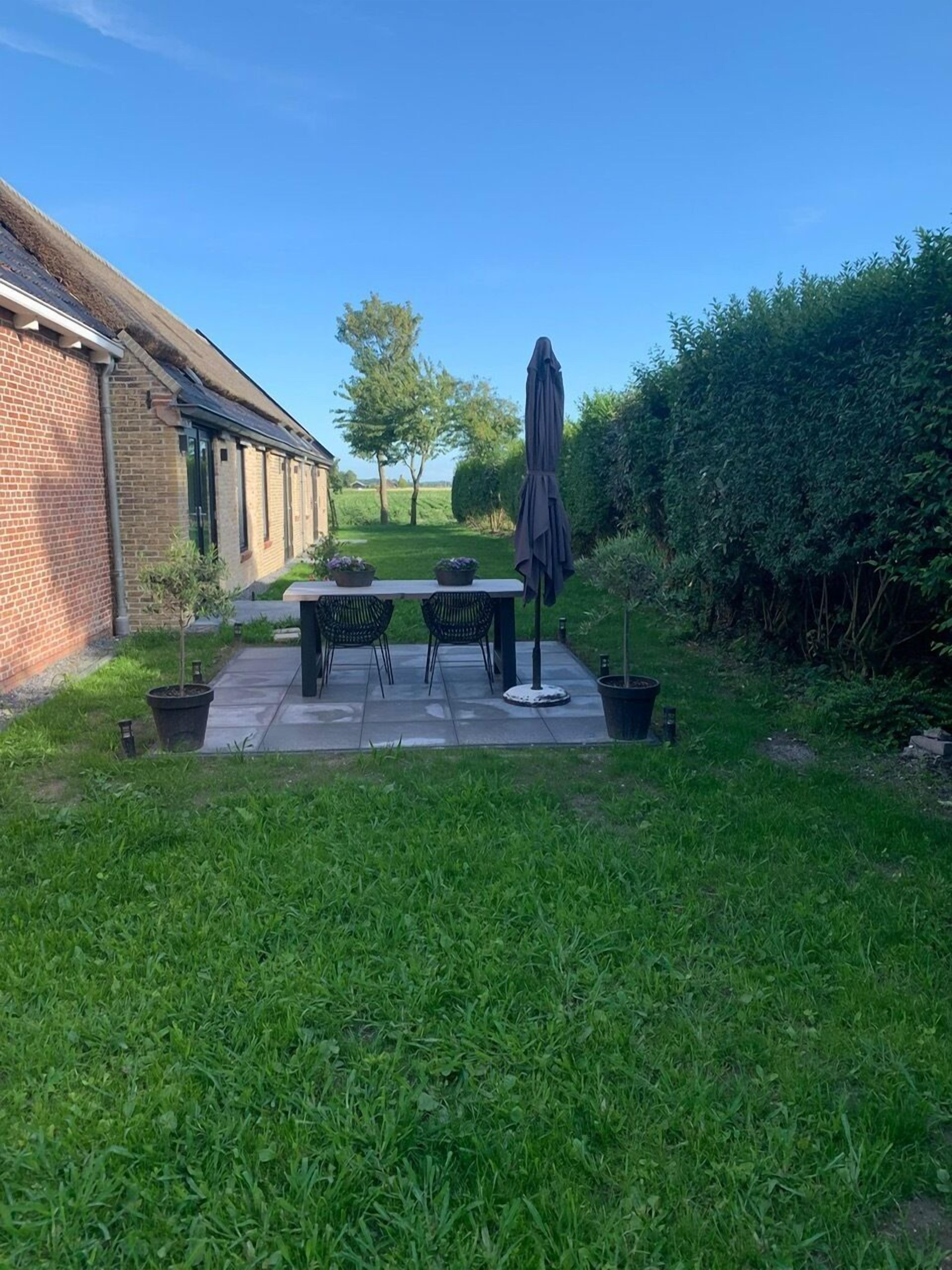 Un patio con una mesa y sillas, rodeado por un seto y un muro de ladrillo.