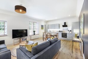 A modern living room with a grey sofa, a TV, and a dining area with a table and chairs. - The Woodside Apartments (Doune)