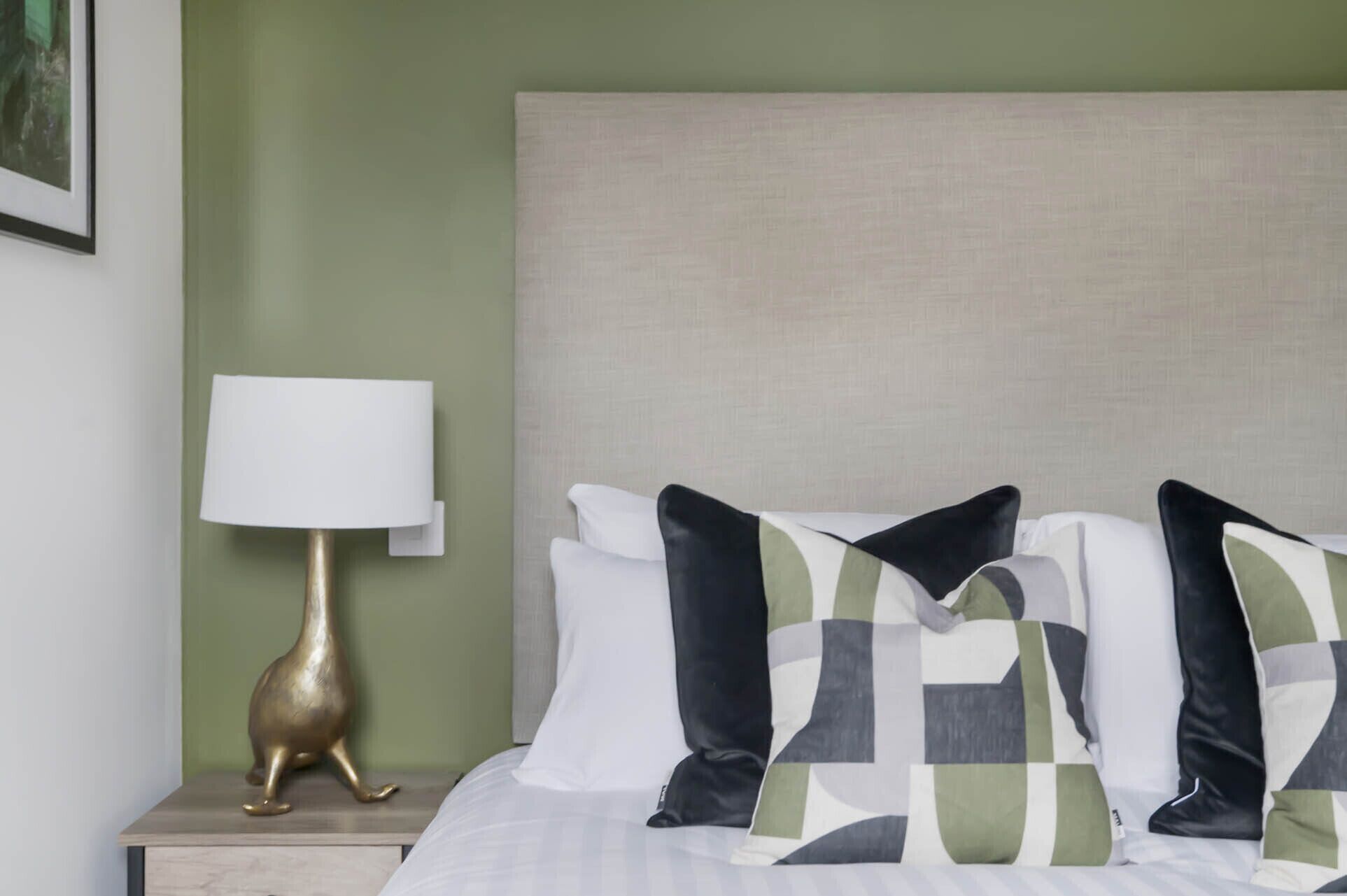 A neatly made bed with a headboard, a bedside lamp, and decorative pillows.