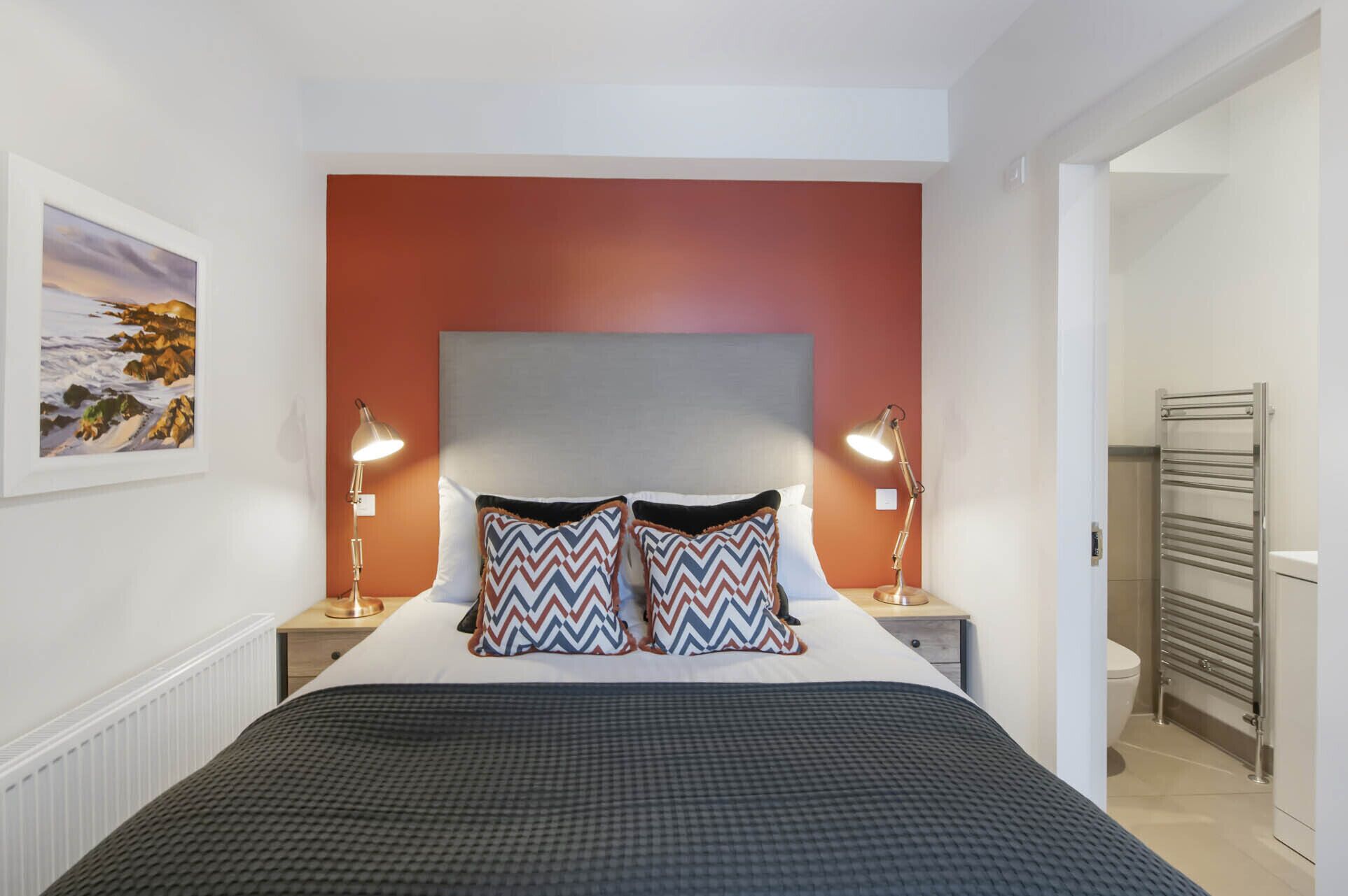 Une chambre d’hôtel avec un lit, deux lampes de chevet, une tête de lit et un tableau au mur.