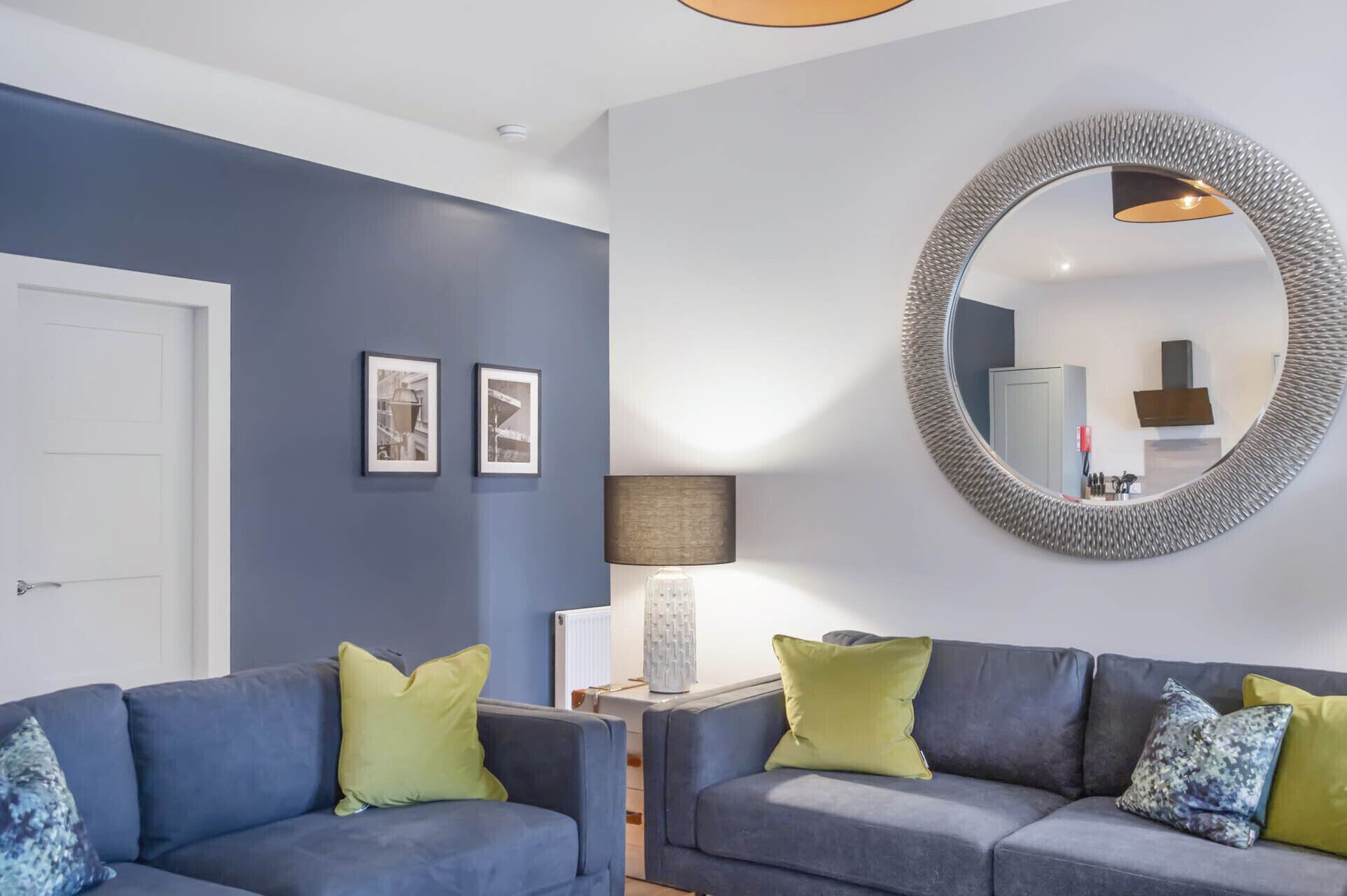 Una sala de estar moderna con un sofá azul, un espejo redondo y dos cuadros en la pared.