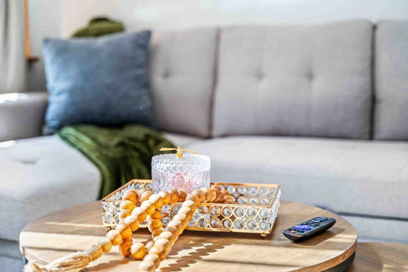 A round wooden table with a remote control, a decorative glass container, and a beaded string.