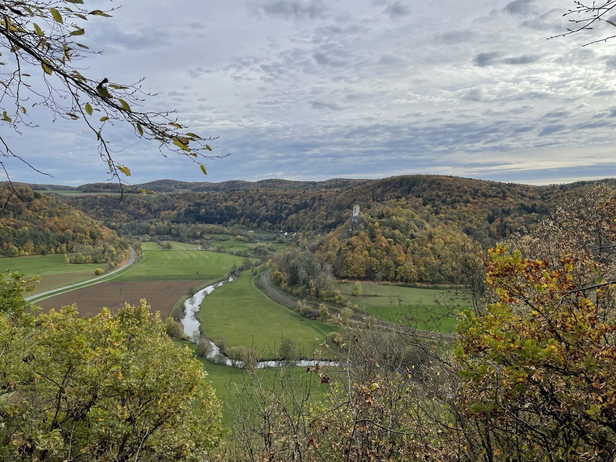 A panoramic view of a valley with a river, surrounded by hills and autumn foliage.