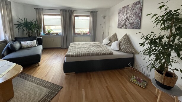 Un dormitorio moderno con cama, sofá, mesa de comedor y un gran ventanal con cortinas.