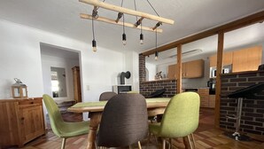 Un comedor con una mesa y sillas de madera, una pared de ladrillo y una cocina al fondo.
