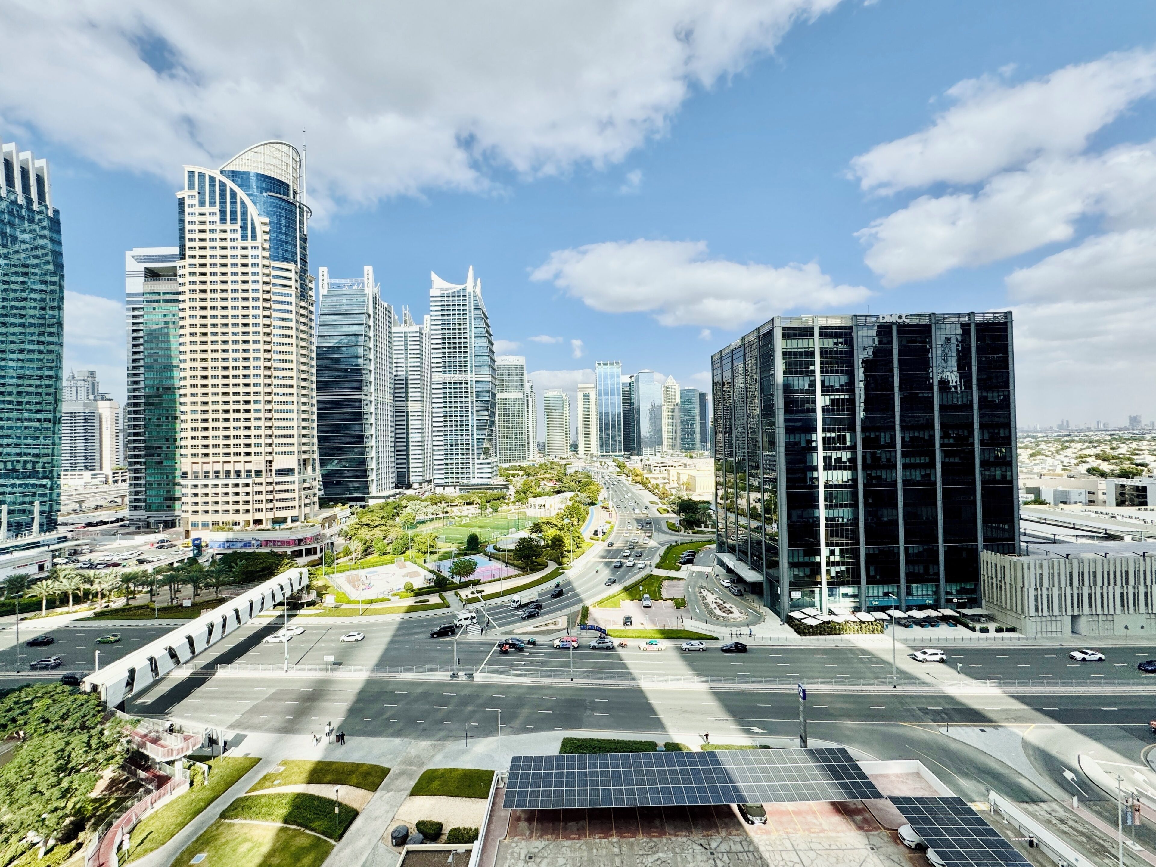 Un paysage urbain moderne avec de hauts immeubles, une large avenue et des espaces verts.