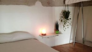 Ein Schlafzimmer mit einem Bett, einem Nachttisch mit Lampe und einer hängenden Pflanze.