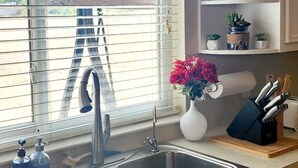 A kitchen with a double sink, a window with blinds, a vase with flowers, and a shelf with decorative items. - Luxurious Ranch at the heart of Round Rock (Round Rock)