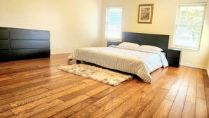 A bedroom with a large bed, wooden flooring, a fluffy rug, and two windows with blinds. - Luxurious Ranch at the heart of Round Rock (Round Rock)