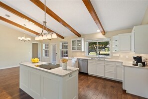 A modern kitchen with white cabinetry, a central island, and a large window providing a view of the outdoors.
