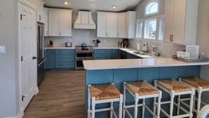 A modern kitchen with white cabinets, a central island with bar stools, and built-in appliances. - Amazing Sunsets & Luxury - Soundfront Pet Friendly Oasis w/ Elevator & Hot Tub (Kitty Hawk)