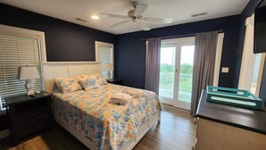 A bedroom with a bed, a nightstand, a dresser, a ceiling fan, and a view of the outdoors. - Amazing Sunsets & Luxury - Soundfront Pet Friendly Oasis w/ Elevator & Hot Tub (Kitty Hawk)