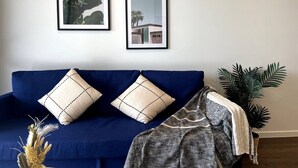 A blue sofa with two pillows, a framed plant, and a framed picture on the wall. - Specious apartment in Kingston, centrally located place. (Kingston)