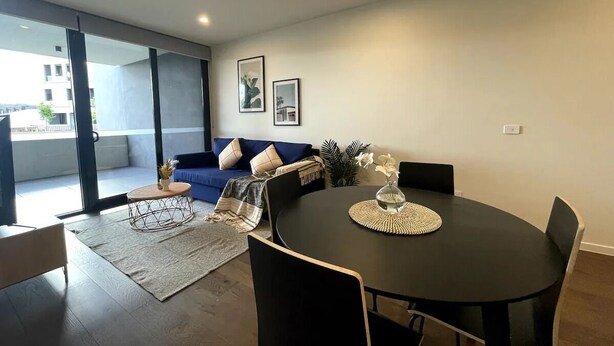 A modern living room with a round black table, a blue sofa with cushions, and a large window offering a view of the outside. - Specious apartment in Kingston, centrally located place. (Kingston)