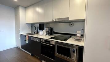 A modern kitchen with stainless steel appliances, white cabinetry, and a black countertop.