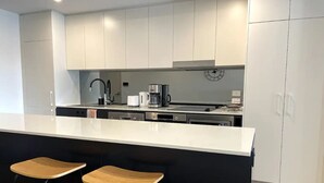 A modern kitchen with white cabinets, a large island with two bar stools, a coffee maker, and a clock on the wall. - Specious apartment in Kingston, centrally located place. (Kingston)