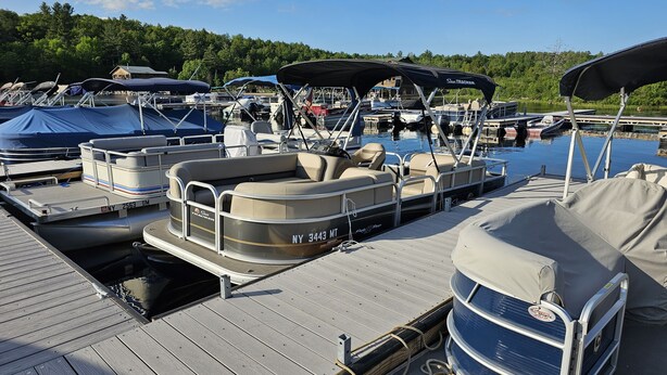 A marina with several boats docked, including a covered pontoon boat and a motorboat. - Dog Friendly, located Between Lake Placid and Saranac Lake with pontoon rentals (Ray Brook)