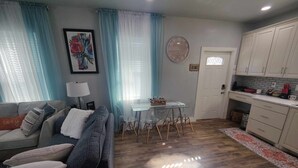 A living room with a sofa, a dining table with chairs, a kitchen area with cabinets, and a clock on the wall. - Family-friendly stand alone apartment in a peaceful Suburb . (Burleson)