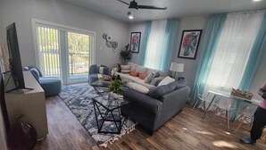 A living room with a grey sofa, a coffee table, a TV, and a dining area with a table and chairs. - Family-friendly stand alone apartment in a peaceful Suburb . (Burleson)