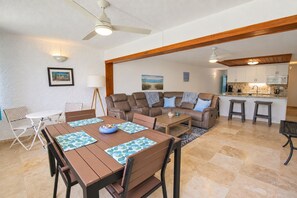 A modern living room with a dining area, a kitchen, and a ceiling fan.