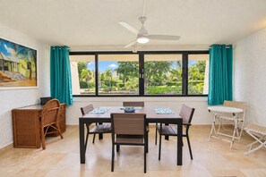 A room with a dining table, chairs, a ceiling fan, and a view of greenery outside.