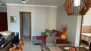 A modern living room with a sofa, a dining table with chairs, and a unique hanging light fixture. - Apto Maravilhoso com Vista Para o Mar, 50mts da Orla da Praia Grande em Ubatuba (Praia Grande Ubatuba)