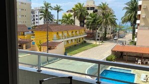 A balcony with a glass table and chairs, overlooking a swimming pool and a residential area with palm trees and buildings. - Apto Maravilhoso com Vista Para o Mar, 50mts da Orla da Praia Grande em Ubatuba (Praia Grande Ubatuba)