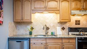 A kitchen with wooden cabinets, a granite countertop, a stainless steel sink, a dishwasher, and a stove. - Downtown 2BR King Bed FREE Parking 1413 (Atlanta)