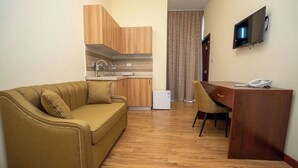Un espacio habitable compacto con sofá, escritorio pequeño, televisión y kitchenette.