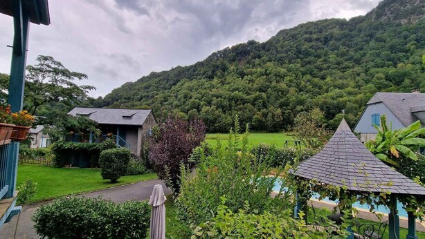 A house with a garden, a small pool, and a view of a forested hill.