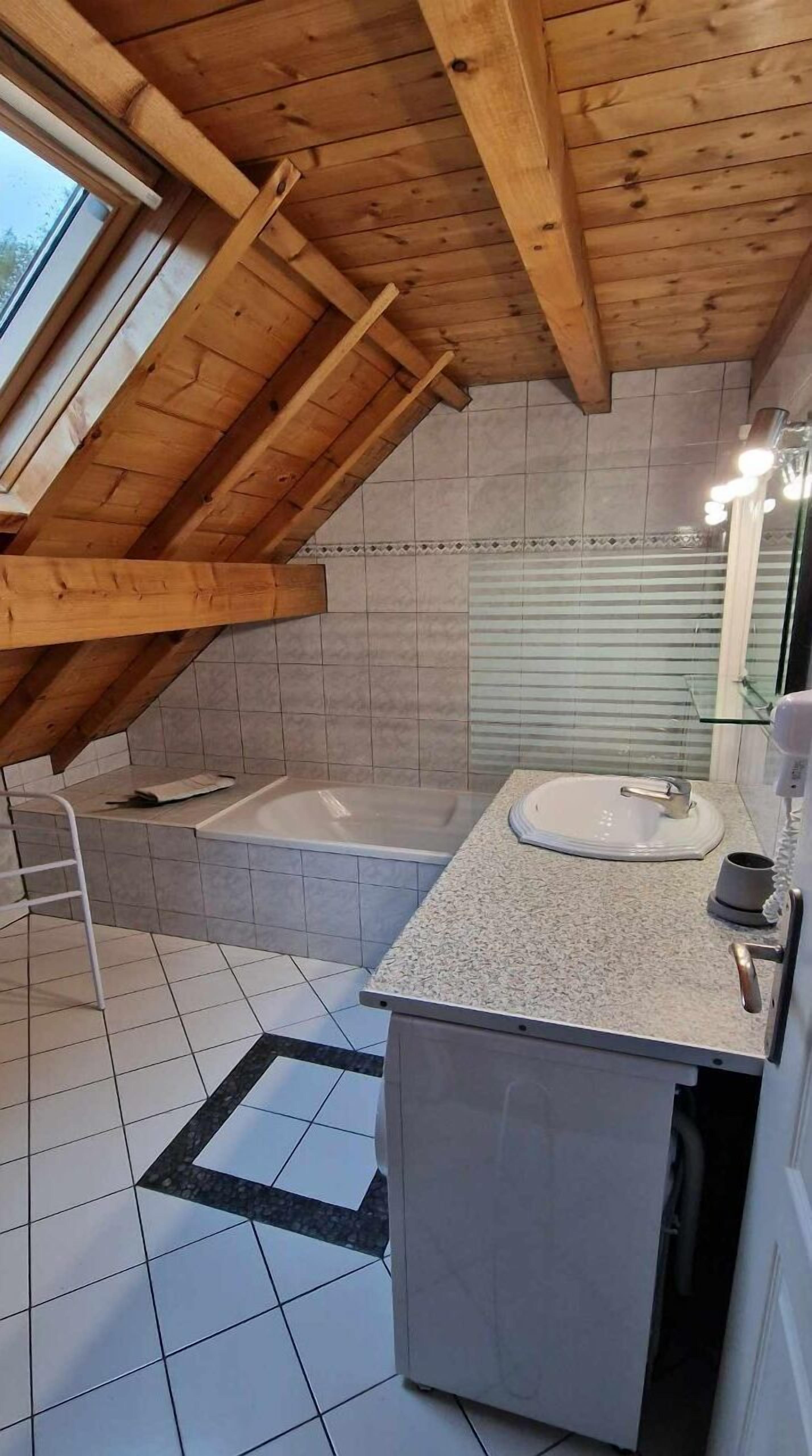 Une salle de bain moderne avec un plafond en pente, une baignoire, un lavabo et un miroir.