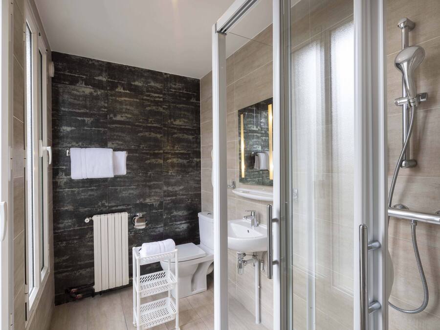 A modern bathroom with a glass shower enclosure, a white sink, and a dark textured wall.