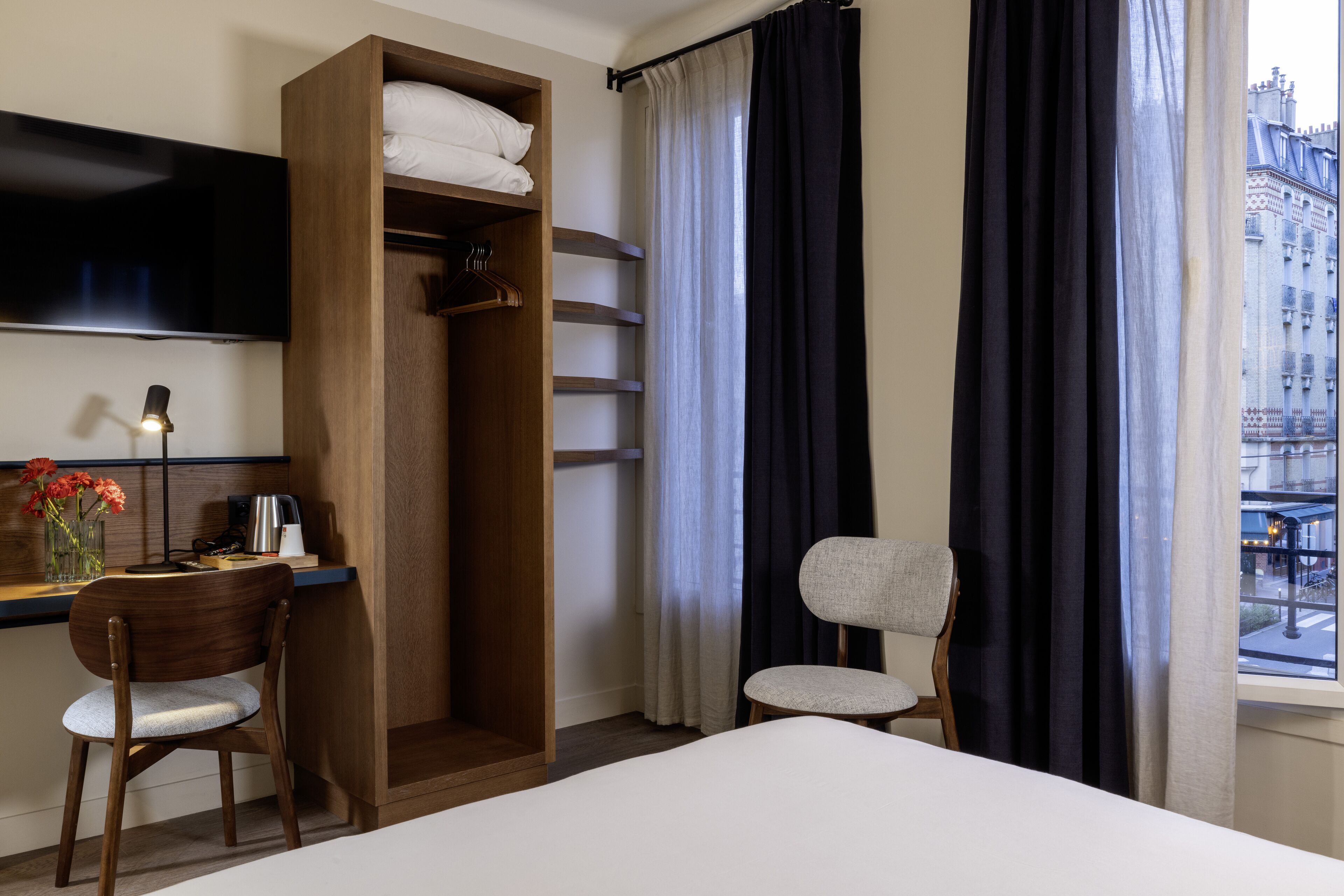 Una camera d'albergo con un letto, una scrivania con una sedia, un armadio, una TV e una finestra con tende.