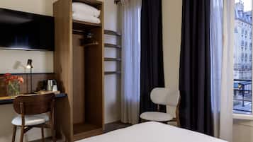 Una camera d'albergo con un letto, una scrivania con una sedia, un armadio, una TV e una finestra con tende.