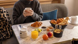 Une table de petit-déjeuner avec des croissants, des fruits et un verre de jus d’orange.