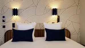 Une chambre d’hôtel avec un papier peint à motifs, deux tables de chevet avec des lampes, un lit avec deux oreillers et une tête de lit.