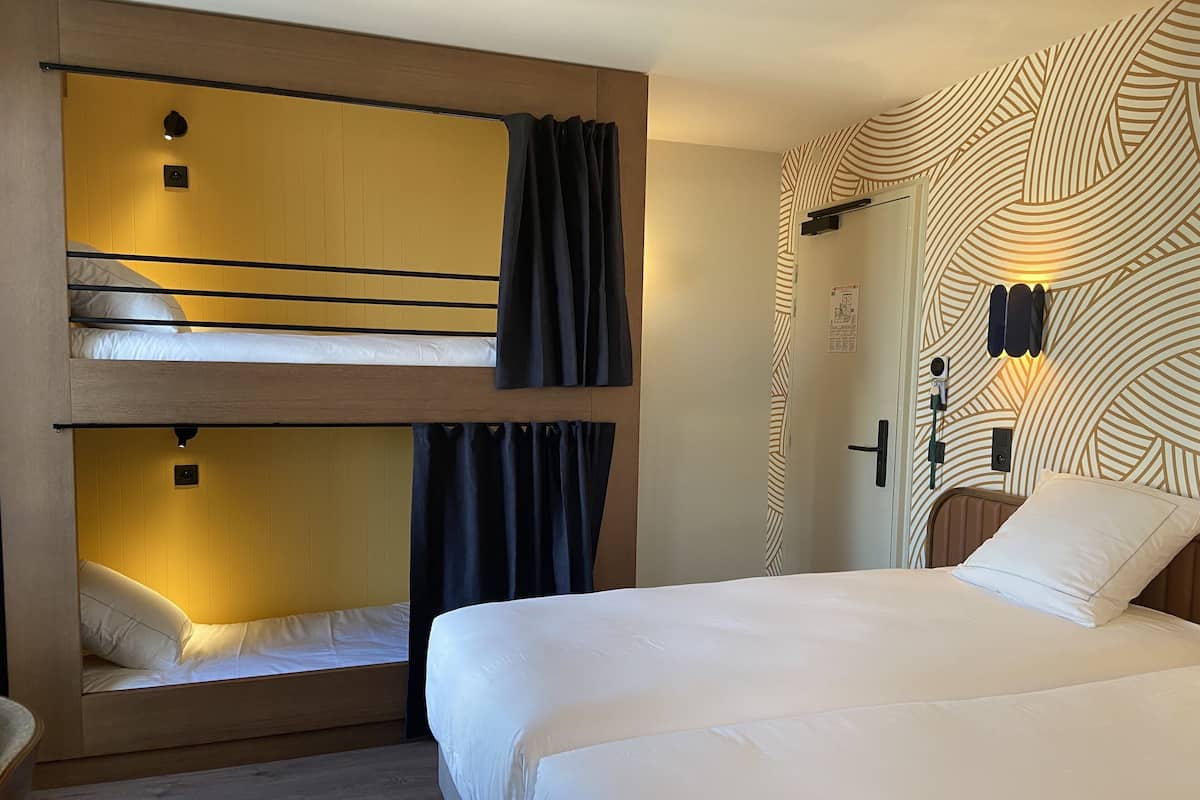 A hotel room with bunk beds, a single bed, a patterned wall, and a door with a handle.