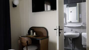 A compact hotel room with a small desk, chair, and a television mounted on the wall.