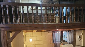 Ein gemütliches Wohnzimmer mit einer Holztreppe, einem weißen Sofa, einem kleinen Tisch mit Blumen in einer Vase und einem Grill draußen.