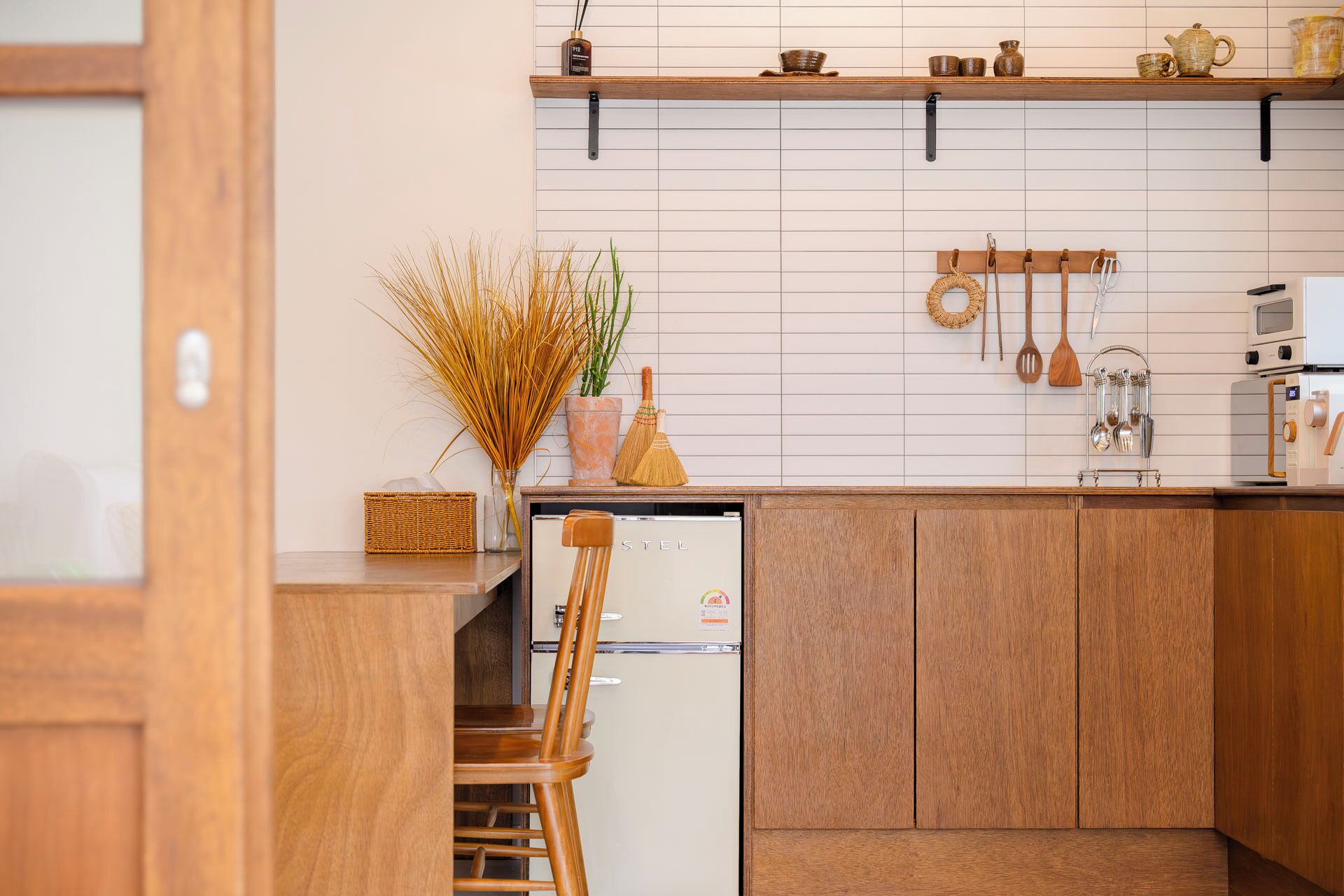 A kitchen with wooden cabinets, a white tiled backsplash, a microwave, and various kitchen utensils hanging on the wall.