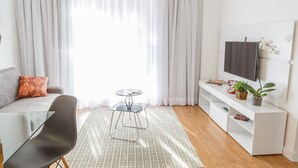A modern living room with a sofa, a glass table, a TV on a white stand, and a potted plant. - Apartamento aconchegante na Praça Pôr do Sol (São Paulo)