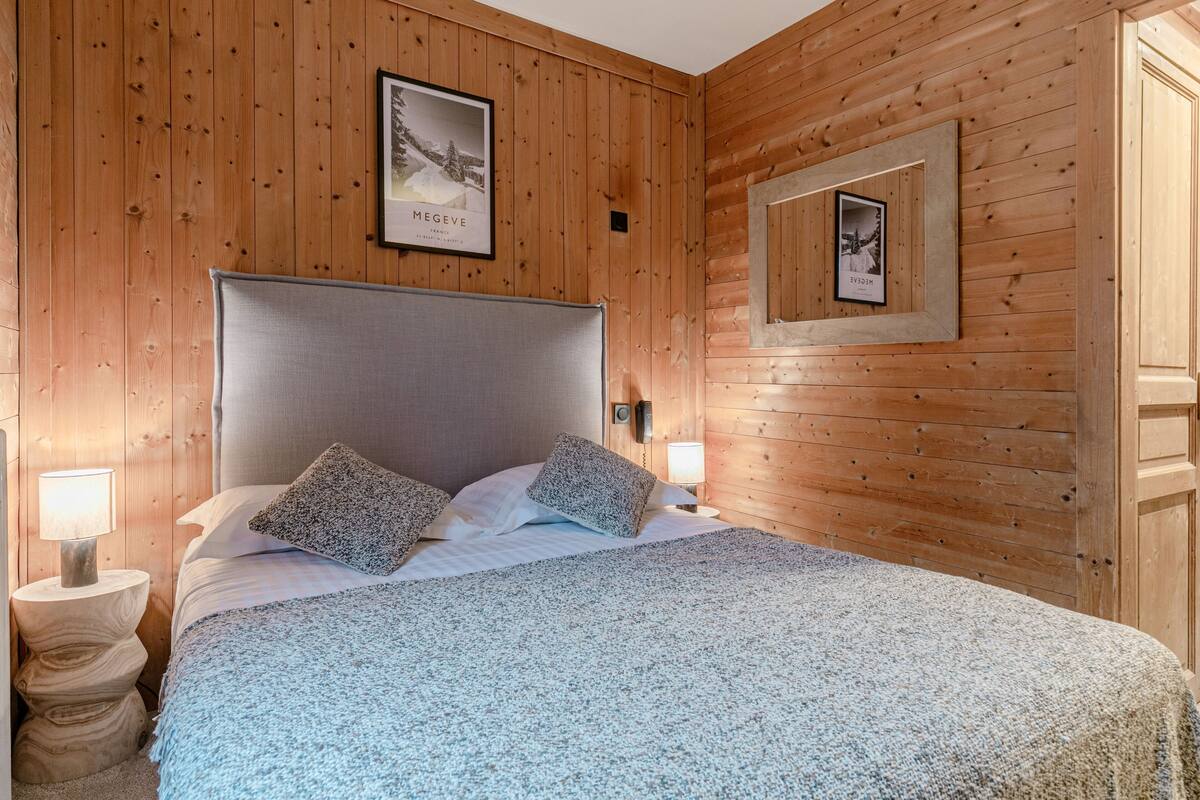 A wooden-paneled bedroom with a large bed, two bedside lamps, and framed pictures on the wall.