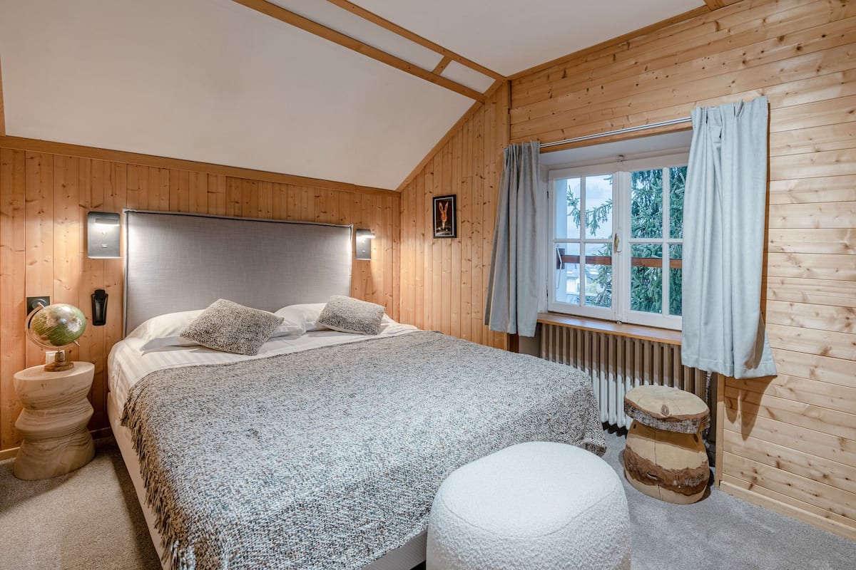 A wooden-paneled bedroom with a bed, a globe on a nightstand, and a window with curtains.