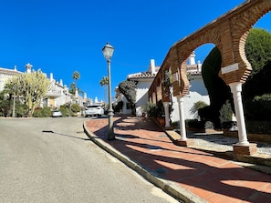 Une rue avec une arche en briques, un lampadaire et un bâtiment blanc portant une enseigne.