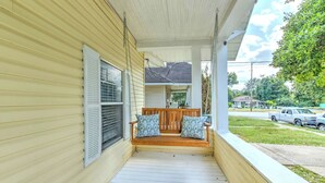 A covered porch with a wooden bench and patterned cushions, a white railing, and a view of a street with parked cars and houses. - Updated Midtown Bungalow • Walk to Cooper-Young Dining • Sleeps 7 • Close to All (Memphis)