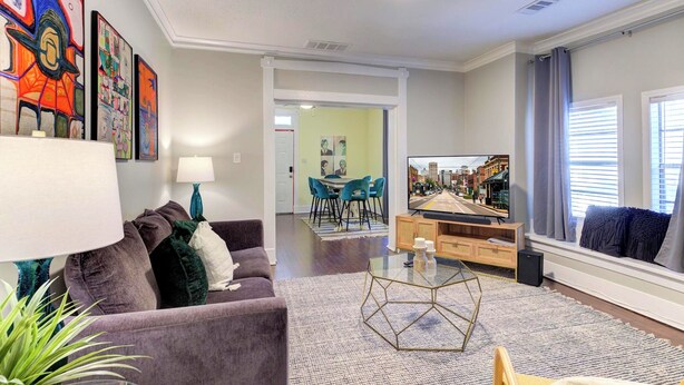 A modern living room with a purple sofa, a glass coffee table, and a dining area with blue chairs. - Updated Midtown Bungalow • Walk to Cooper-Young Dining • Sleeps 7 • Close to All (Memphis)