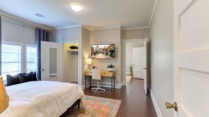 A bedroom with a bed, a desk, and a chair. There is a window with blinds and a door leading to another room. - Updated Midtown Bungalow • Walk to Cooper-Young Dining • Sleeps 7 • Close to All (Memphis)