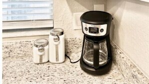 A kitchen with a coffee maker, a bread box, and a window with blinds.