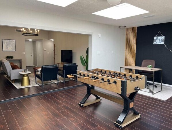 A living room with a foosball table, a sofa, a coffee table, and a TV.